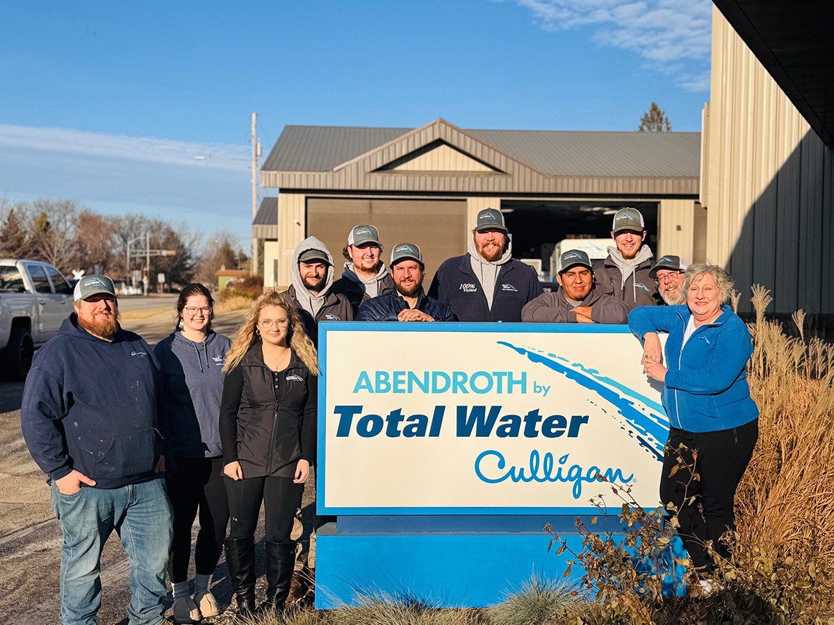Abendroth Water staff posing for photo around sign